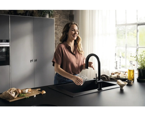 Frau spült Glas in schwarzer Küchenspüle mit passender Armatur