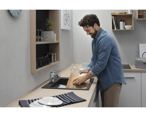 Mann spült Geschirr in einer modernen Küche mit Spüle und Armatur