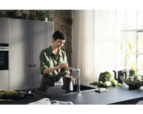 Frau befüllt Wasserkanne an einer Küchenarmatur in einer modern eingerichteten Küche.