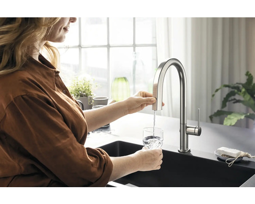 Frau füllt Wasser aus einer Küchenarmatur in ein Glas