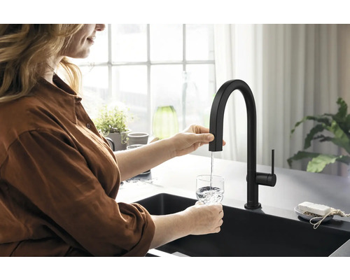 Eine Person füllt ein Glas Wasser mit einer schwarzen Küchenarmatur in einer hellen Küche.