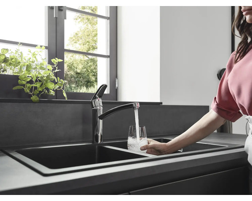 Küchenszene mit Doppelspüle, Armatur und Person, die ein Glas mit Wasser füllt