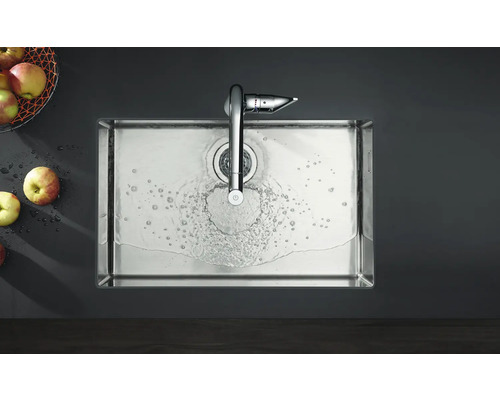 Edelstahlspüle mit Wasserhahn und laufendem Wasser, zusammen mit Äpfeln in einem Korb