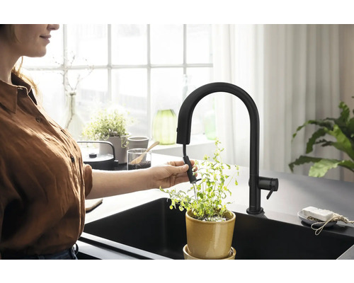 Frau gießt Pflanze mit schwarzer Küchenarmatur mit Ausziehbrause