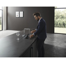 Mann spült Glas in moderner Küche mit Spültischarmatur