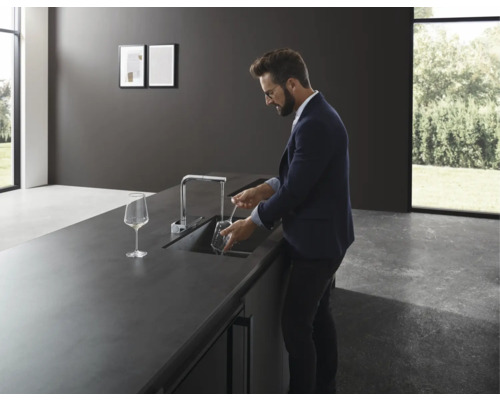 Mann spült Glas in moderner Küche mit Spültischarmatur