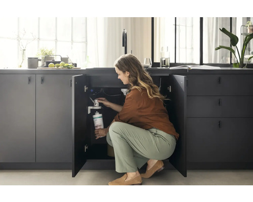 Frau installiert einen Wasserfilter unter der Spüle in einer grauen Küche.