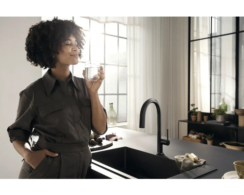 Frau trinkt Wasser am Spültisch mit Wasserhahn in einer hellen Küche.