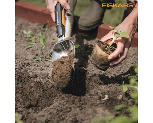 Gartenarbeitsszene mit einer Person, die eine Pflanze mit einer Edelstahlschaufel der Marke Fiskars in die Erde setzt