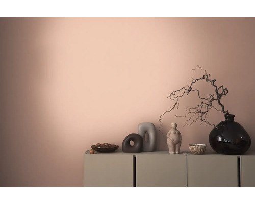 Dekoratives Interieur mit einer Kommode, Vasen und Skulpturen vor einer farbigen Wand.