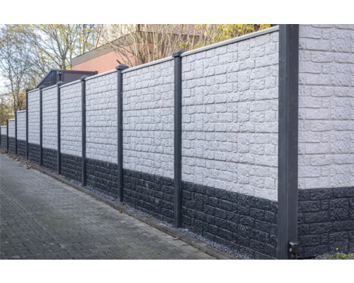 Eine lange, graue Lärmschutzwand mit Pfosten begrenzt ein Grundstück.