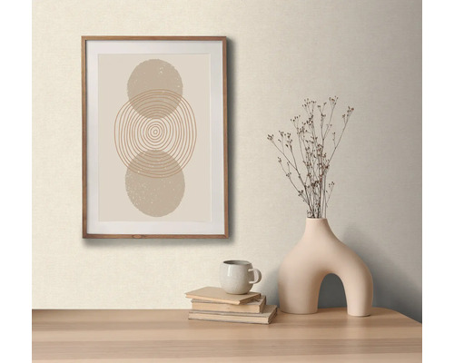 Dekoratives Arrangement mit einem gerahmten Bild mit abstraktem Kreismotiv, einer Vase mit Trockenblumen, einer Tasse und Büchern auf einem Tisch.