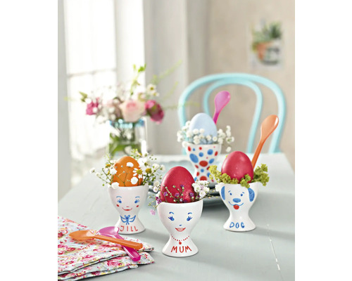 Dekorativer Tisch mit bemalten Ostereiern in Eierbechern, verziert mit kleinen Blumen und Löffeln