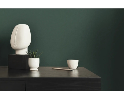 Dekorative Szene mit Skulptur, Pflanze, Tasse und Stift auf einem dunklen Tisch vor einer grünen Wand