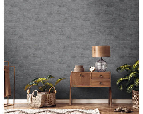 Wohnzimmer mit grauer Strukturtapete, Holzkommode, Tischlampe und Zimmerpflanzen.
