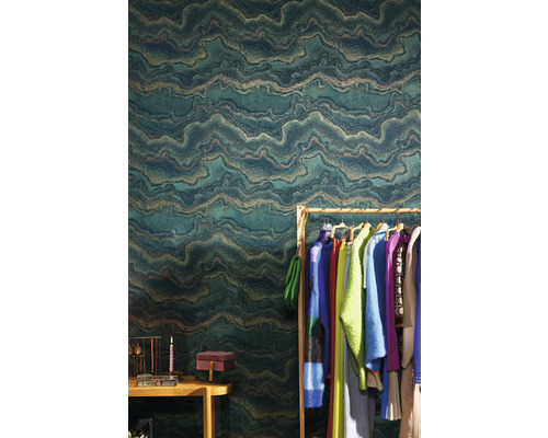 Wohnszene mit einer grünen Vliestapete mit wellenförmigem Muster, Kleiderständer und Accessoires