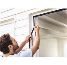 Eine Person befestigt eine Fensterdichtung an einem Fensterrahmen.