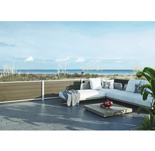 Moderne Terrasse mit hellgrauem Ecksofa für den Außenbereich, Holztisch und dunklen Bodenfliesen vor einer Küstenlandschaft mit Meerblick.