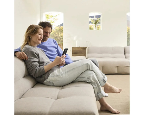 Paar sitzt auf einem Sofa und schaut auf ein Mobiltelefon in einem hellen Wohnzimmer.