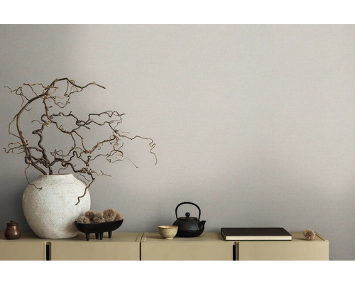 Nahaufnahme einer dekorierten Kommode mit Vase, Ästen und Teekanne vor einer beigen Wandtapete.