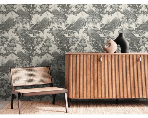 Dekoratives Zimmer mit einer Tapete, die Pfauen und Blumen zeigt, einem Holzschrank und einem Stuhl aus Rattan.