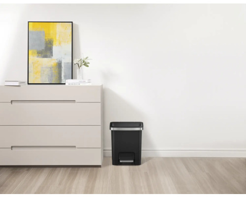 Zimmer mit Kommode, Dekoration und einem schwarzen Treteimer.