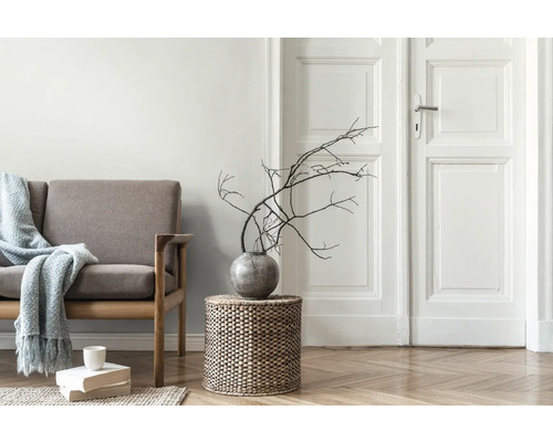 Wohnzimmer mit Sofa, Beistelltisch aus Korbgeflecht, Vase mit Ästen und Bücherstapel