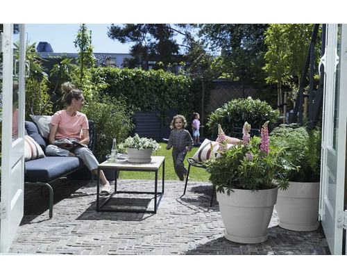 Szene im Garten mit Frau auf einer Bank, spielenden Kindern und bepflanzten Blumentöpfen