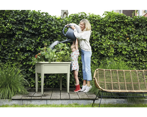 Eine Frau gießt mit ihrer Tochter einen Kräutergarten in einem Hochbeet im Garten.