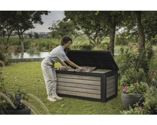 Eine Frau räumt eine Gartenbox im Garten ein. Die Gartenbox ist aus Holz und Kunststoff.