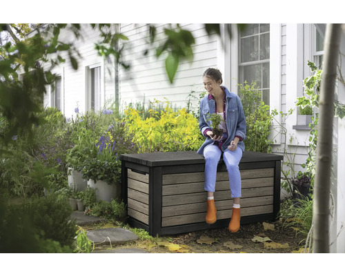 Frau sitzt auf einer wetterfesten Aufbewahrungsbox im Garten