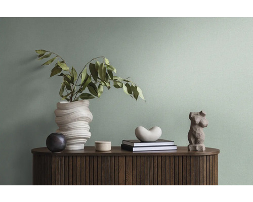 Dekorative Gegenstände auf einem Holzschrank, darunter eine Vase mit Zweigen, Bücher und eine Skulptur