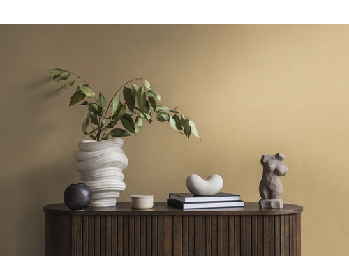 Dekorative Szene auf einem dunklen Holzschrank mit einer weißen Vase, grünen Blättern, Büchern und Statuen.