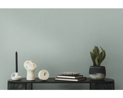 Dekorative Szene auf einem schwarzen Regal mit Kerze, Skulptur, Uhr, Büchern und einer Topfpflanze vor einer Wand.
