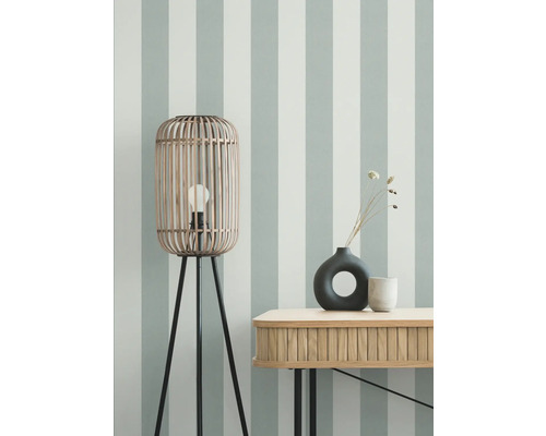 Raumansicht mit Stehlampe aus Holz, Tisch und Dekoration vor gestreifter Wand