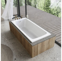 Weisse Badewanne auf einer Holzverkleidung in einem Badezimmer mit grosser Fensterfront und Natur im Hintergrund.