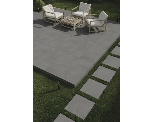 Terrasse mit grauen Fliesen, Sitzgruppe mit Holzrahmen und weißen Polstern sowie Trittplatten im Rasen.