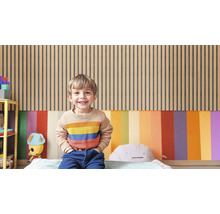 Ein Kind sitzt vor einer Wand mit Holzpaneelen und farbigen Flächen