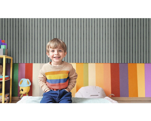Ein lächelnder Junge sitzt in einem Kinderzimmer mit gestreifter Tapete und farbenfroher Wandgestaltung.