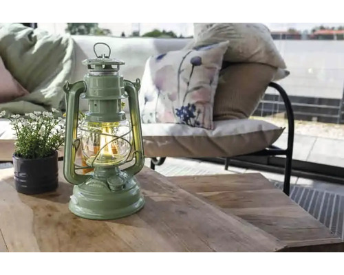 Dekorative Laterne auf einem Holztisch mit Topfpflanze und Sitzgruppe im Hintergrund.