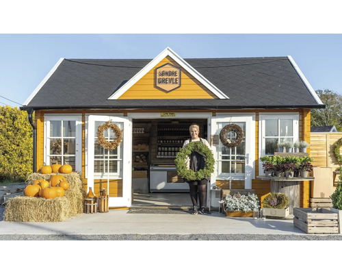 Ein gelbes Gartenhaus mit einem Frau, die einen Kranz hält und Kürbisse davor.