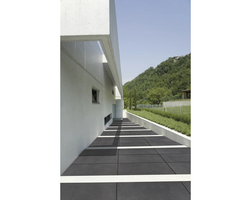 Außenbereich mit grauen Bodenplatten, einem weißen Gebäude und einer grünen Hügellandschaft