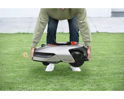 Eine Person hebt einen Rasenmähroboter auf einer Rasenfläche an.