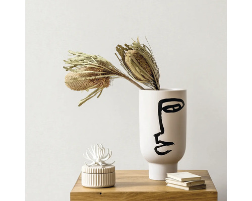 Dekorative Vase mit Gesichtsmuster und getrockneten Blumen auf einem Tisch
