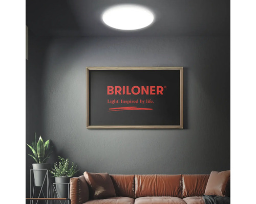 Wohnzimmer mit runder Deckenleuchte und gerahmtem Briloner Logo an der Wand über dem Sofa