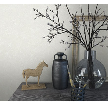 Dekorative Anordnung mit Vase, Zweigen, Pferdefigur und Pinsel auf einem Tisch.