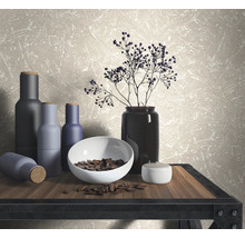 Dekorative Szene mit Vasen, Schale und Zweigen auf einem Tisch vor einer Wandtapete.