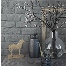 Dekorative Szene mit Vase, Zweigen, Pferdefigur und Behälter mit Pinseln auf einem Tisch vor einer Ziegelwand
