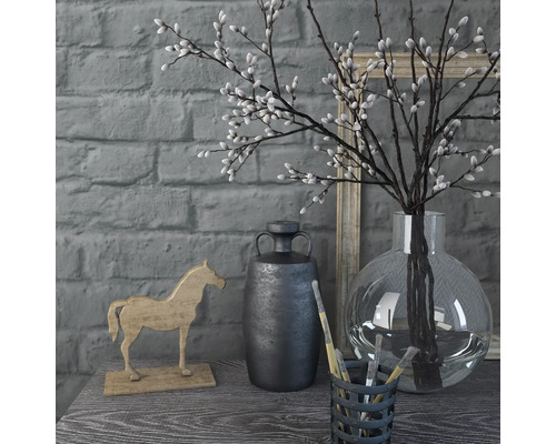 Dekorative Szene mit Vase, Zweigen, Pferdefigur und Behälter mit Pinseln auf einem Tisch vor einer Ziegelwand