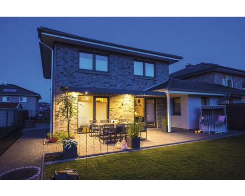 Haus mit Terrasse, Gartenmöbeln und Rasenmähroboter bei Dämmerung